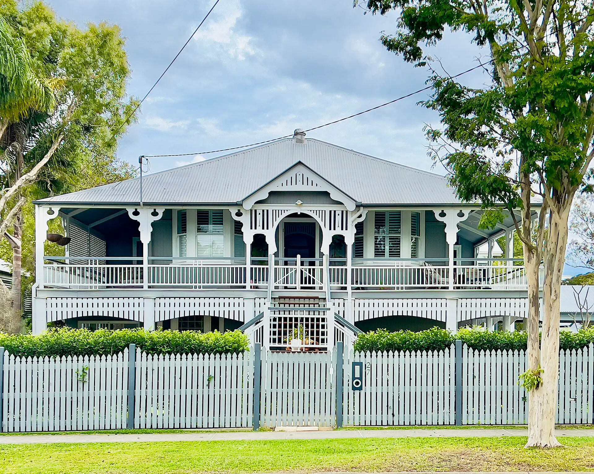 Two-storey Queenslander home with white verandahs and picket fence in Brisbane